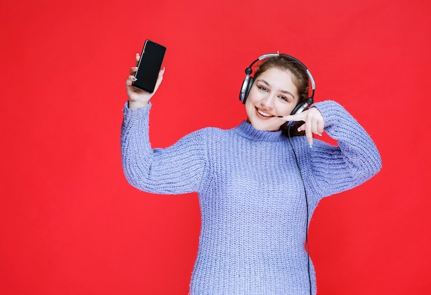 Chica con auriculares demostrando su teléfono inteligente y sintiéndose feliz.