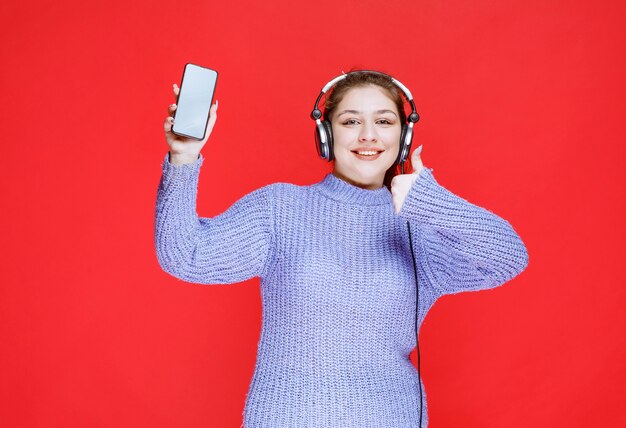 Chica con auriculares demostrando su teléfono inteligente y sintiéndose feliz.