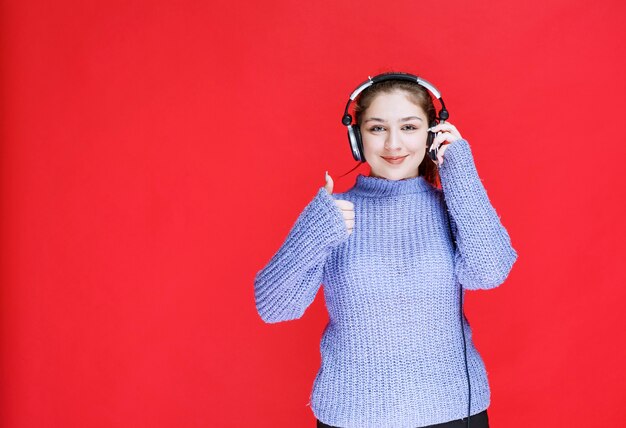 Chica con auriculares disfrutando de la música y mostrando un signo de mano positivo.