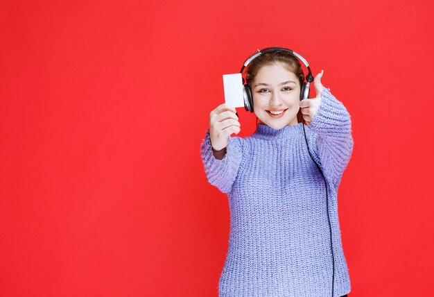 Chica con auriculares mostrando su tarjeta de visita y haciendo el signo de satisfacción.