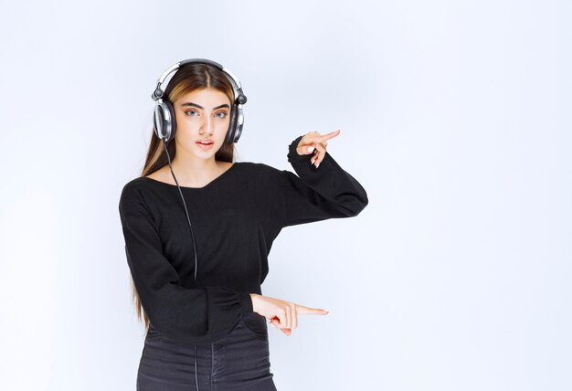 Chica con auriculares mostrando el tamaño de un objeto. Foto de alta calidad