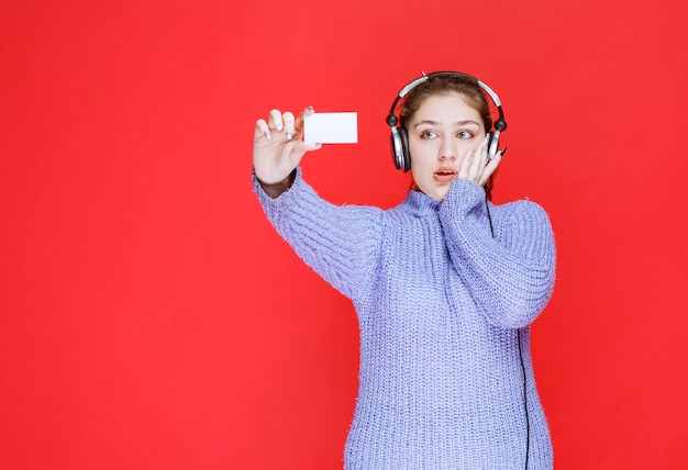 Chica con auriculares sosteniendo una tarjeta de visita y parece sorprendida.