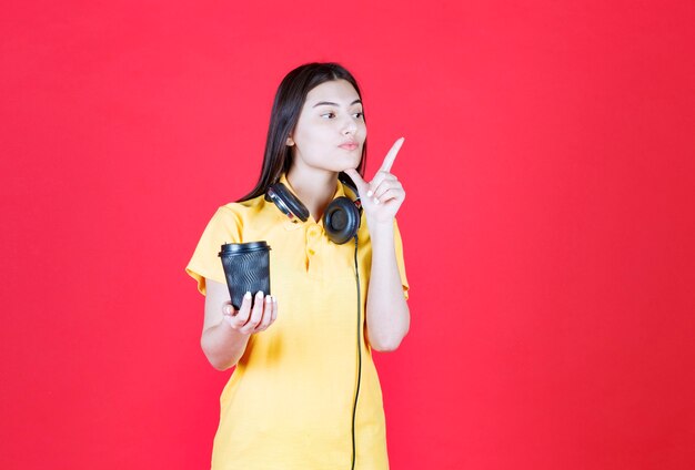 Chica con auriculares sosteniendo una taza de bebida desechable negra.