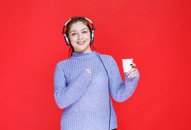 Chica con auriculares sosteniendo una taza de café desechable.