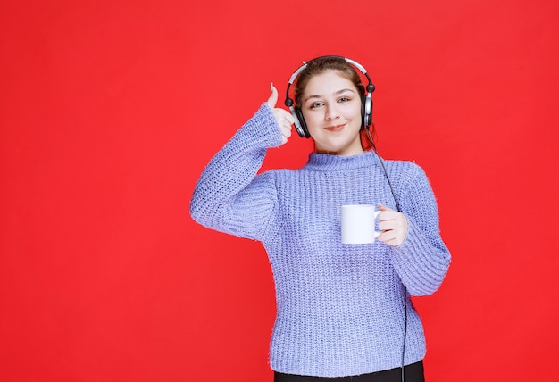 Chica con auriculares sosteniendo una taza de café y sonriendo.