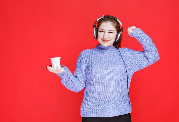 Chica con auriculares tomando café y sintiéndose poderosa.