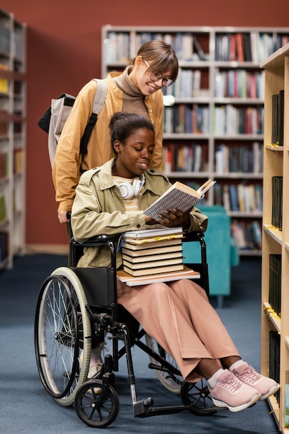 Chica ayudando a su colega en silla de ruedas a elegir un libro para un proyecto