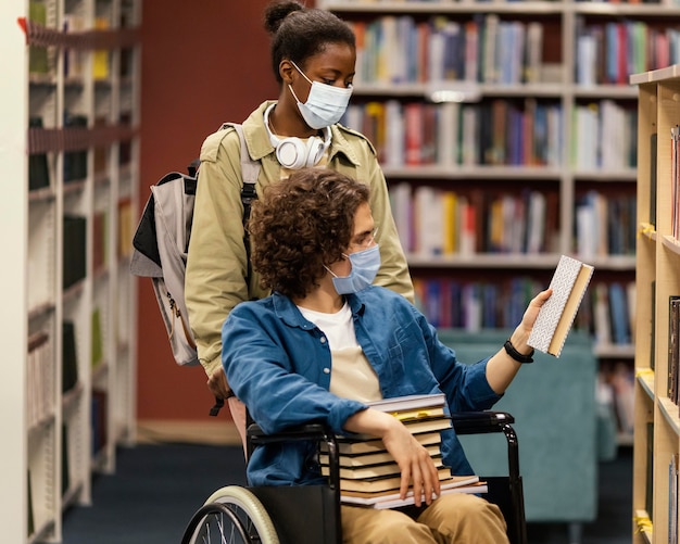 Chica ayudando a su colega en silla de ruedas a elegir sus libros en la biblioteca