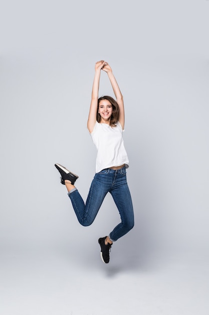 Chica bailando con cabello largo castaño y feliz expresión facial sonriente saltando en estudio aislado en blanco