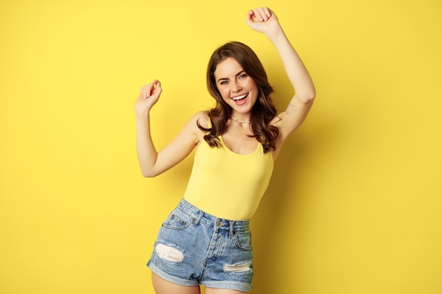 Foto gratuita chica bailando feliz verano divirtiéndose levantando las manos y regocijándose de pie en camiseta sin mangas y pantalones cortos...