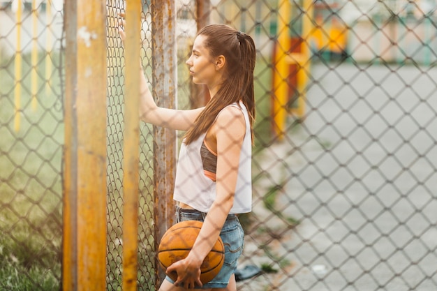 Chica con baloncesto al lado de valla