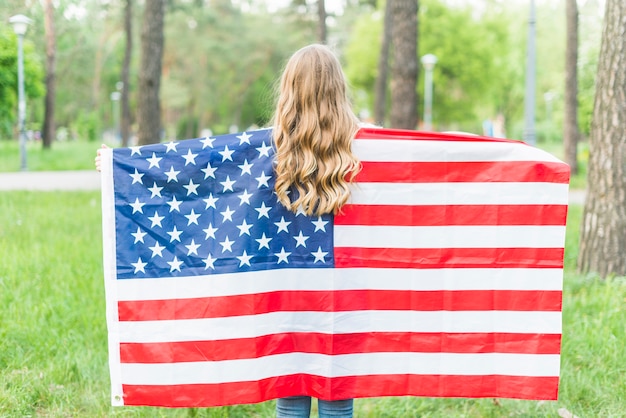 Chica con bandera americana en la naturaleza de detrás