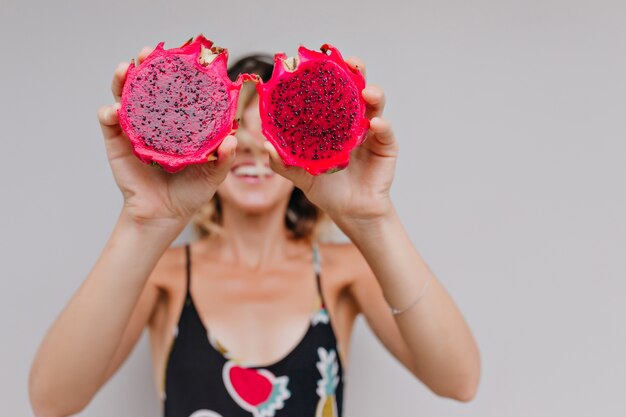 Chica bastante bronceada con pitaya roja. retrato de modelo de mujer relajada posando con frutas de dragón.