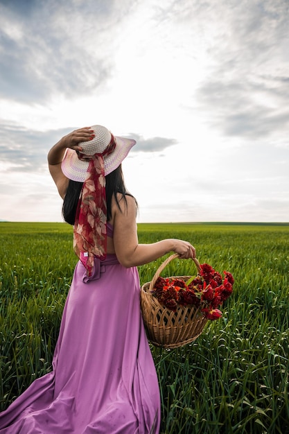 Chica bastante caucásica con un vestido morado sosteniendo una cesta de flores sobre un fondo verde borroso