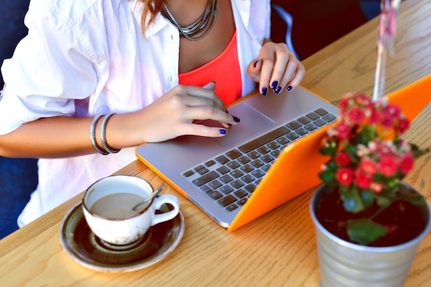 Chica bastante hipster trabajando en su computadora portátil en el café de la ciudad, lugar de coworking, joven freelancer tap en el cuaderno, ambiente de verano.
