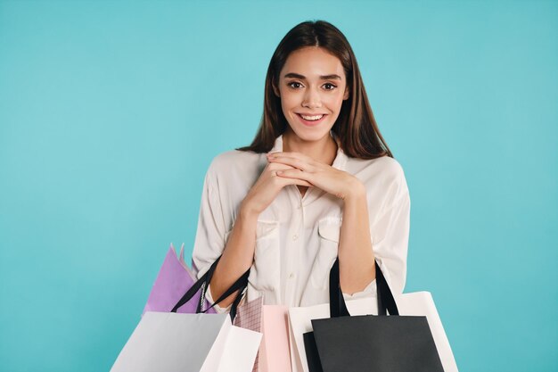 Chica bastante positiva con bolsas de compras felizmente mirando en cámara sobre fondo colorido