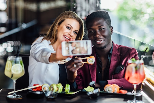 Chica bastante rubia tomando una foto por el teléfono celular con sushi y mojito.