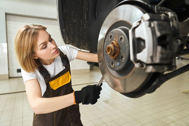 Chica en batas de fijación de disco de freno de coche, utilizando la herramienta.