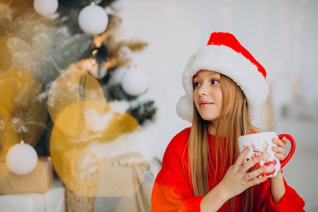 Chica bebiendo cacao por árbol de Navidad