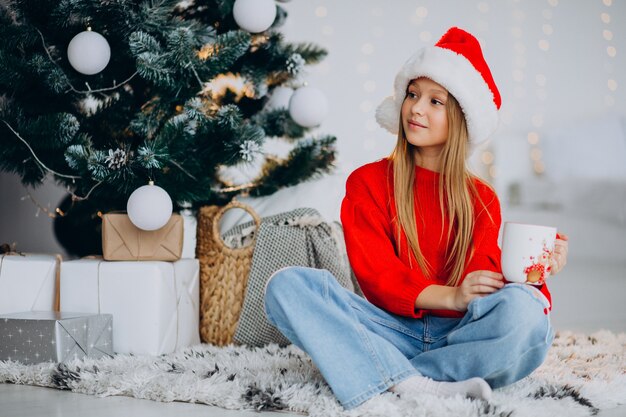 Chica bebiendo cacao por árbol de Navidad