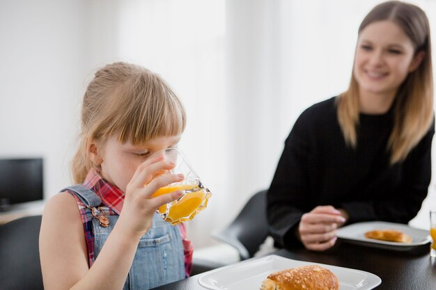 Chica bebiendo jugo cerca de mamá