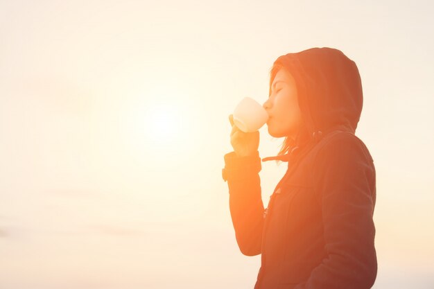 Chica bebiendo de una taza en el atardecer