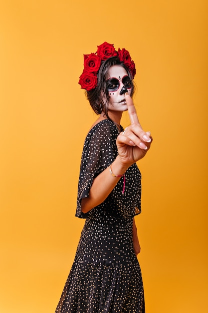 Foto gratuita chica de belleza latina con maquillaje en forma de imagen tradicional de calavera pide permanecer en silencio, mostrando el dedo índice