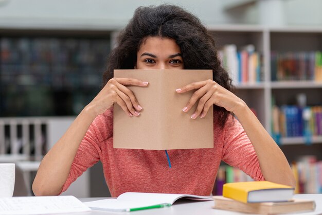 Chica en la biblioteca cubriéndose la cara con el libro