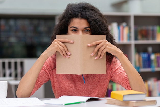 Chica en la biblioteca cubriéndose la cara con el libro