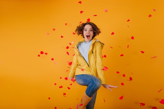 Chica bien vestida bailando, rodeada de corazones rojos. Foto interior de la hermosa modelo femenina morena celebrando el día de San Valentín.