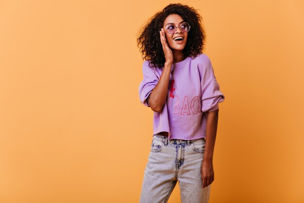 chica bien vestida mirando a su alrededor con una sonrisa. Mujer africana rizada romántica sonriendo en naranja.