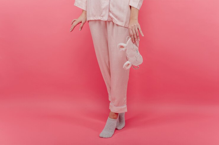 Foto gratuito chica blanca delgada en calcetines lindos de pie de puntillas y sosteniendo antifaz. foto interior de una bella dama en ropa de dormir de algodón con antifaz posando en una pared rosa.