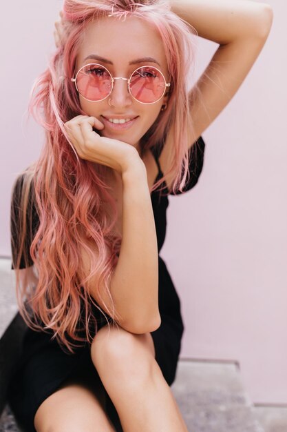 Una chica blanca entusiasta con una sonrisa feliz posando al aire libre sobre un fondo claro Foto de una mujer romántica alegre con el pelo largo y rosa