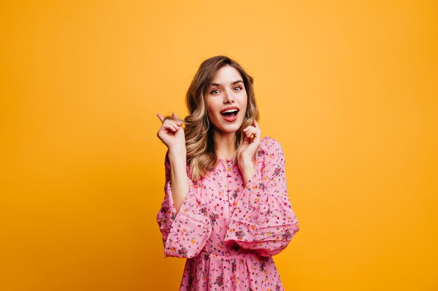 Chica blanca interesada con peinado ondulado que expresa interés. Foto interior de magnífica mujer romántica en vestido rosa.