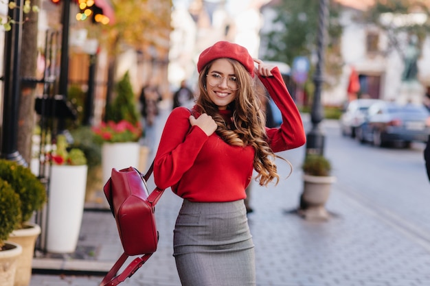 Chica blanca de pelo largo con expresión de cara feliz posando en la calle en un cálido día de otoño