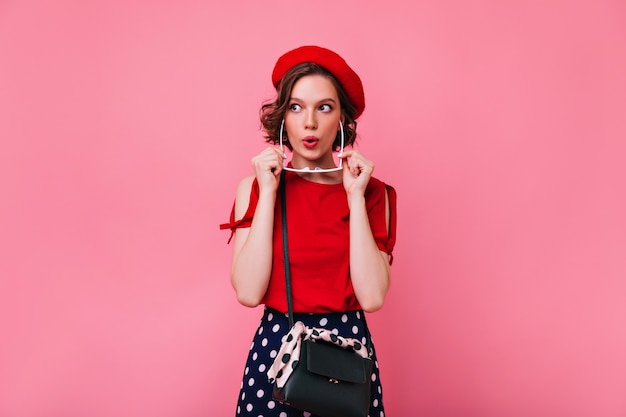 Chica blanca positiva en linda boina roja expresando interés. Foto interior de elegante modelo femenino francés con corte de pelo corto.