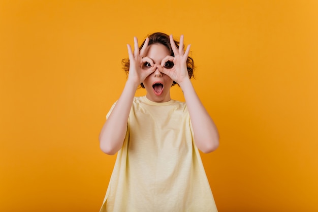 Chica blanca sorprendida en camiseta de gran tamaño jugando mientras posa para la foto. Retrato de interior de magnífica mujer refinada haciendo muecas.