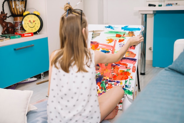 Foto gratuita chica de blanco sentada en el suelo y pintando con gouache sobre lienzo.