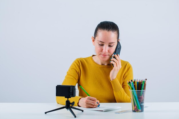 Chica blogger está escribiendo texto hablando por móvil sobre fondo blanco.