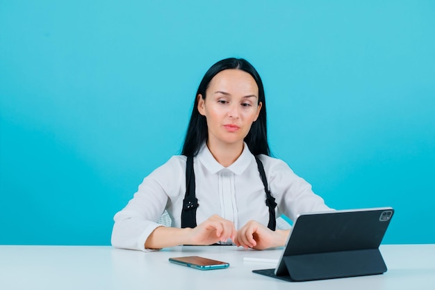 Chica blogger está mirando hacia abajo sentada frente a la tableta sobre fondo azul