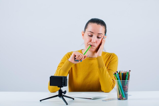 Chica blogger está mirando el bloc de notas sosteniendo un lápiz en los labios sobre fondo blanco.