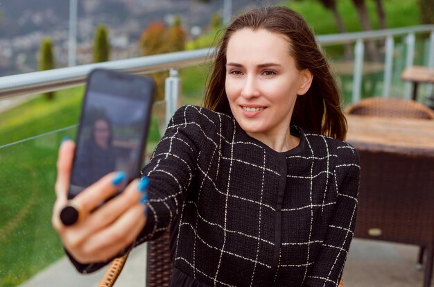 La chica blogger está mirando la cámara trasera del teléfono inteligente en el fondo de la vista de la naturaleza