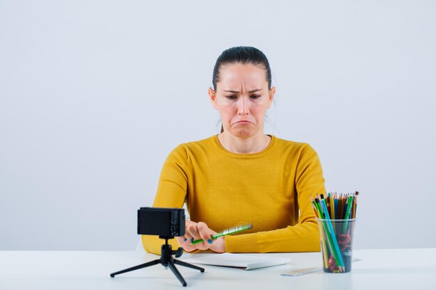 Chica blogger está mostrando mimetismo llorando al sentarse sobre fondo blanco.