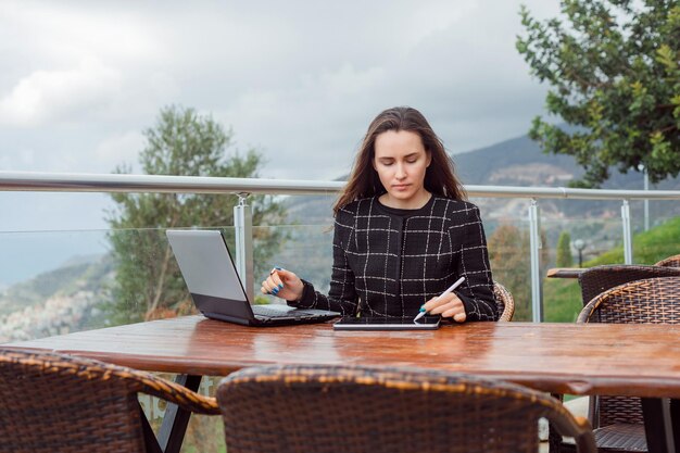 Chica blogger está trabajando en una computadora portátil sentada en el fondo de la vista de la naturaleza