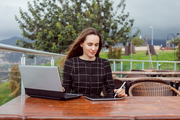 La chica blogger está trabajando en línea en una computadora portátil sentada en el fondo de la vista de la naturaleza