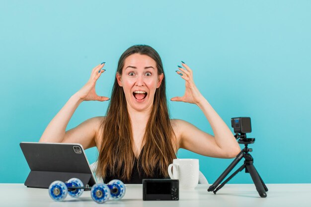 Chica blogger gritando está posando en la cámara mostrando garras sobre fondo azul.