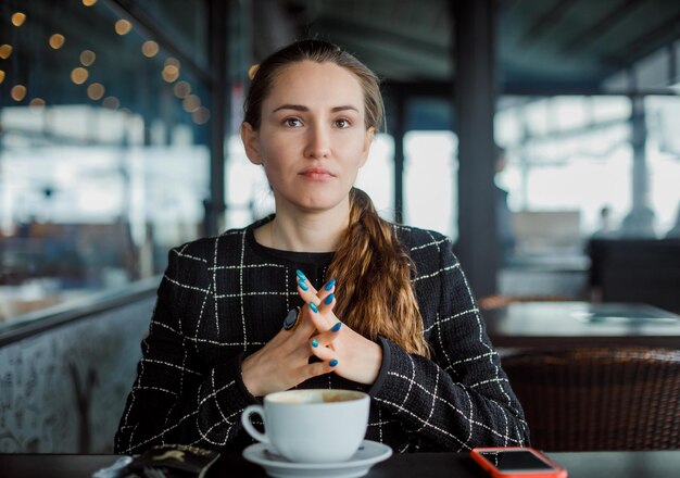 Chica bloguera está mirando a la cámara conectando sus dedos en el café