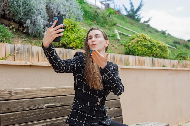 Chica bloguera se está tomando selfie con su teléfono inteligente lanzando un beso en el parque