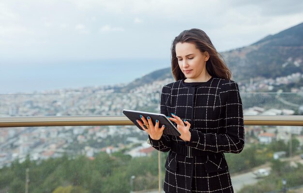 Chica bloguera está usando una computadora planshet para sus trabajos en línea en el contexto de la vista de la ciudad