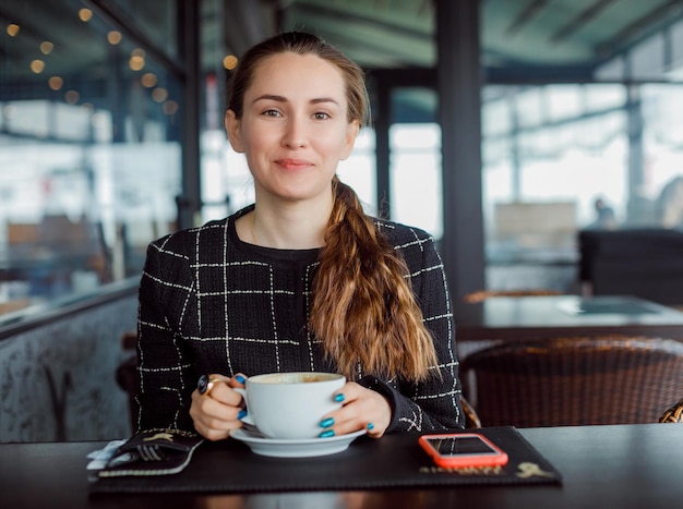 Chica bloguera sonríe sosteniendo una taza de café en la cafetería